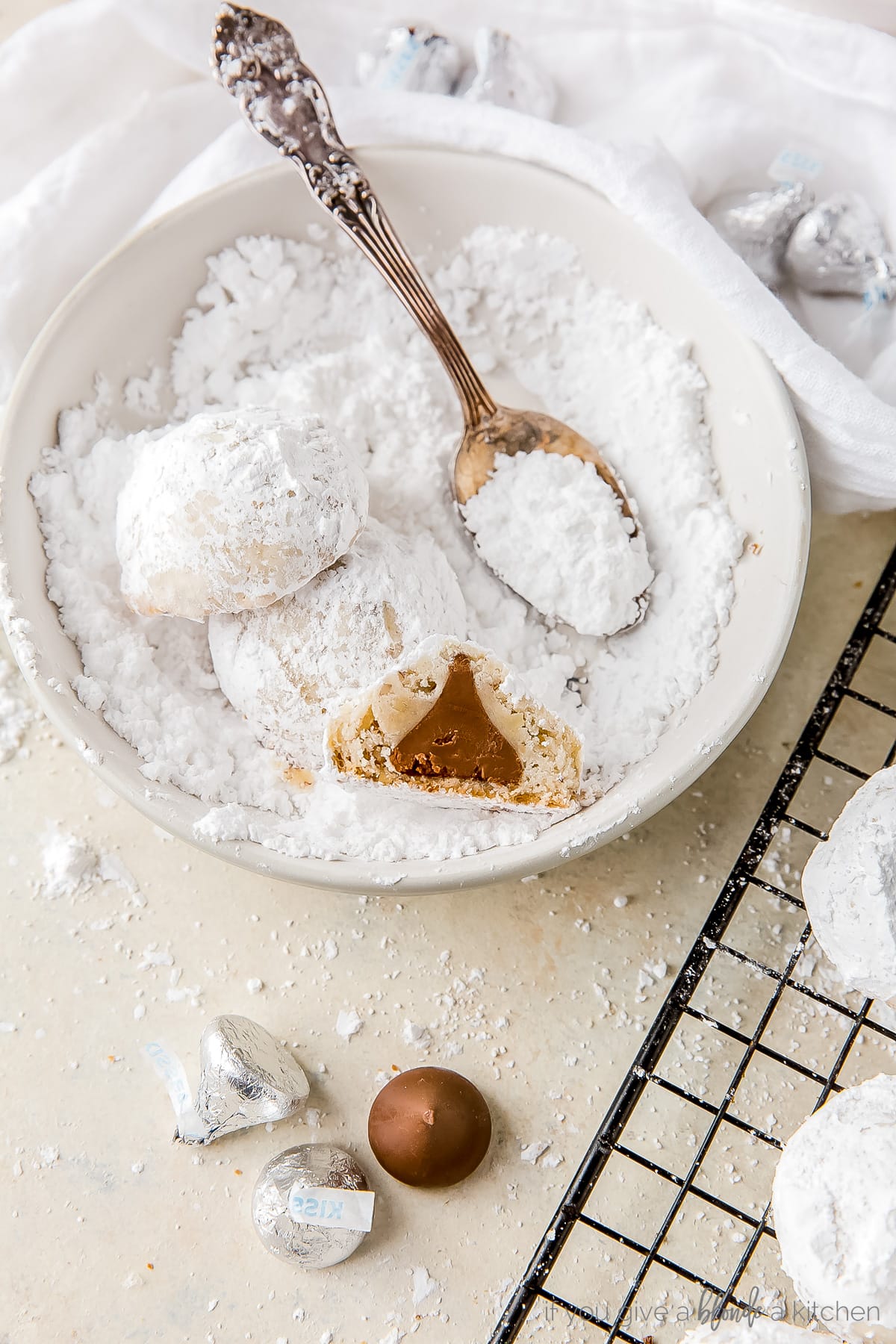 half of surprise kiss cookie in a bowl of confectioners' sugar with a spoon
