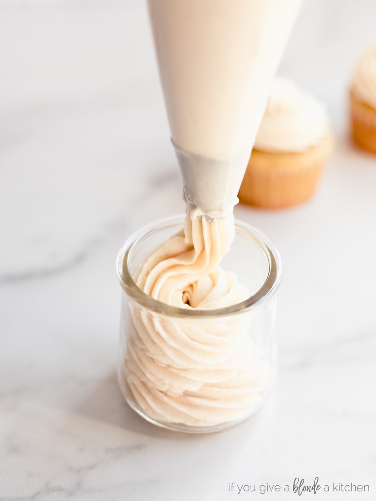 frosting bag piping buttercream frosting into glass jar.