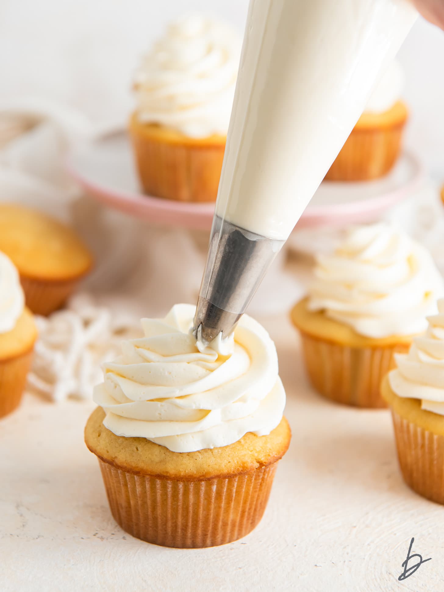 bag of frosting with tip adding buttercream onto vanilla cupcake