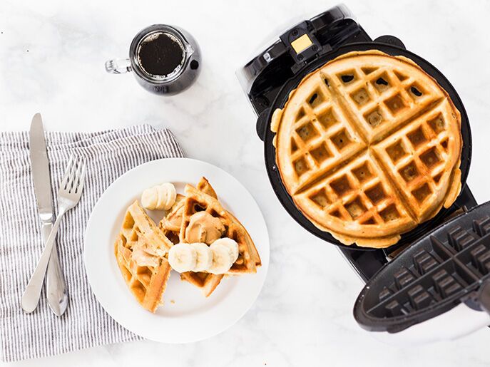 waffle in waffle iron next to plate with stack of banana peanut butter waffles