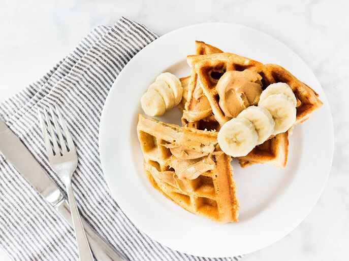 waffles on round white plate. Peanut butter and banana slices on top