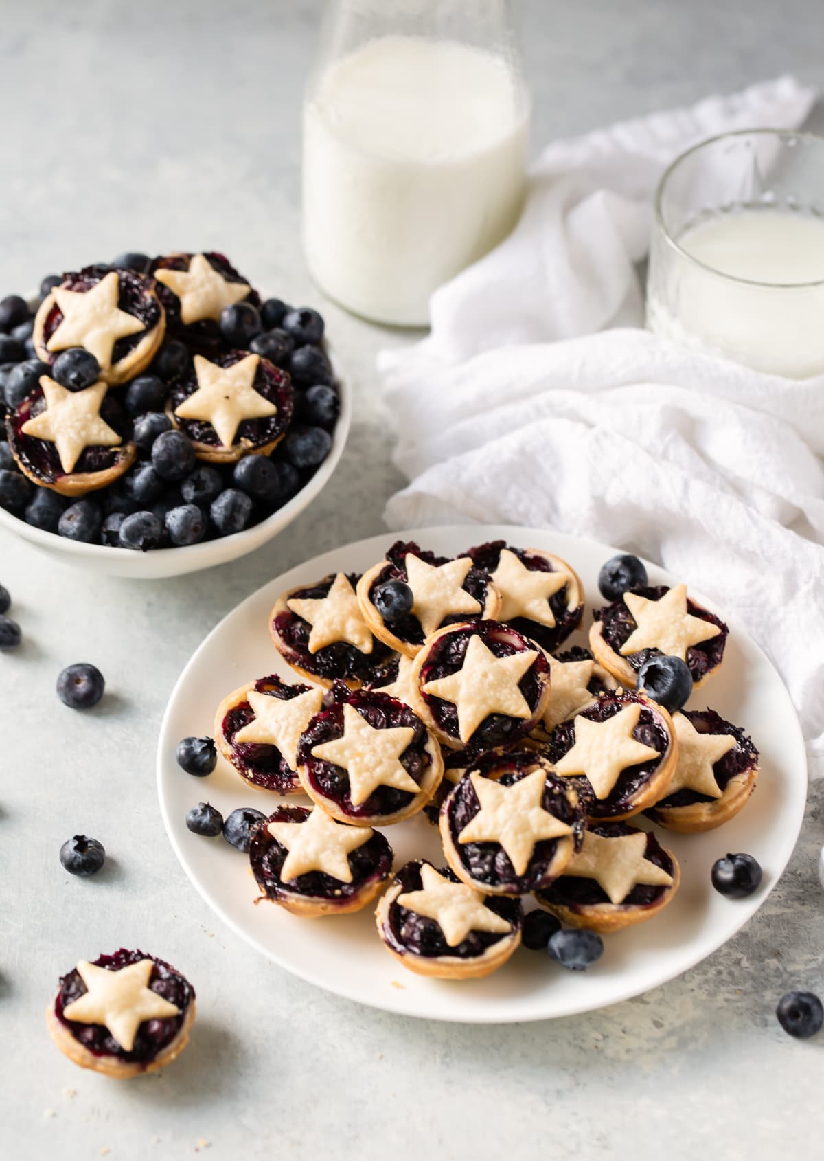 plate of mini blueberry pies next to bowl of blueberries with pies on top