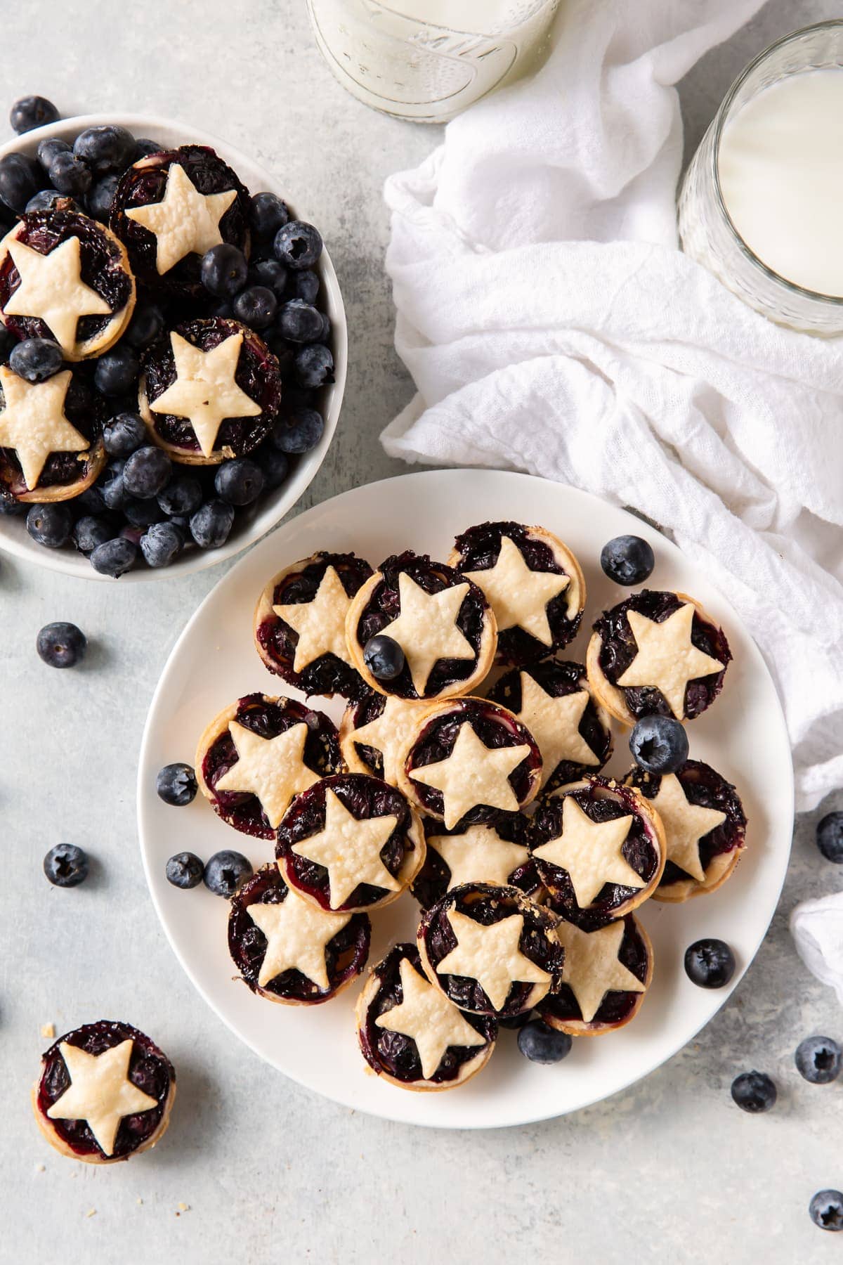 plate of mini blueberry pies next to bowl of blueberries with pies on top