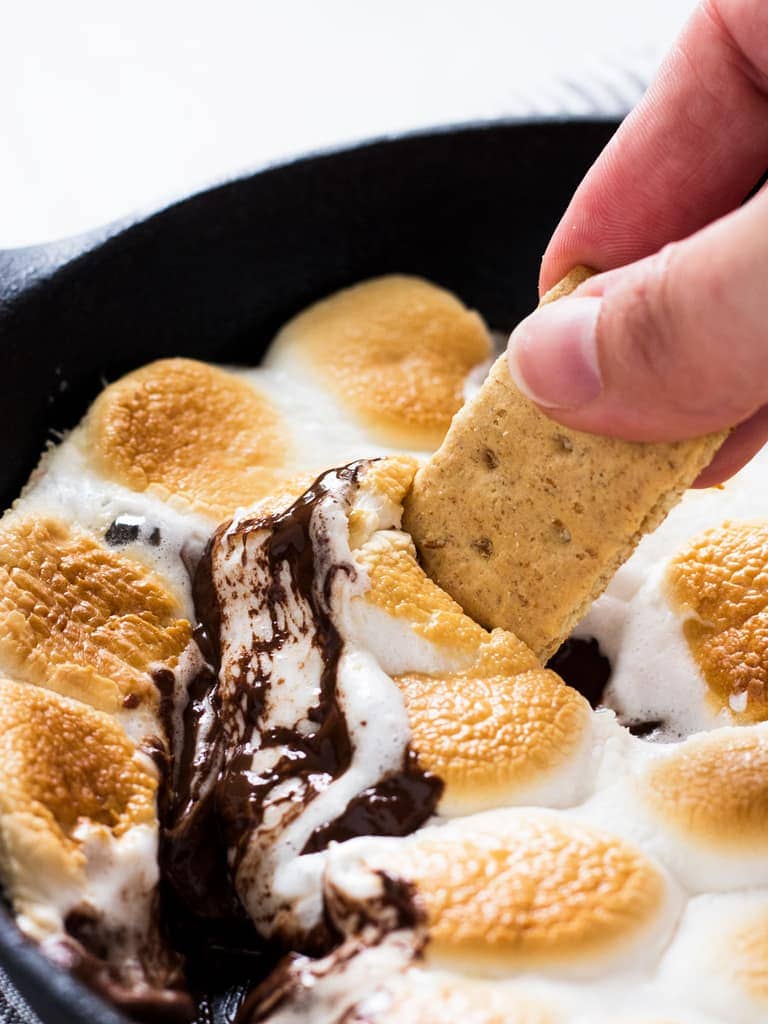 hand dipping graham cracker in melted marshmallow and chocolate