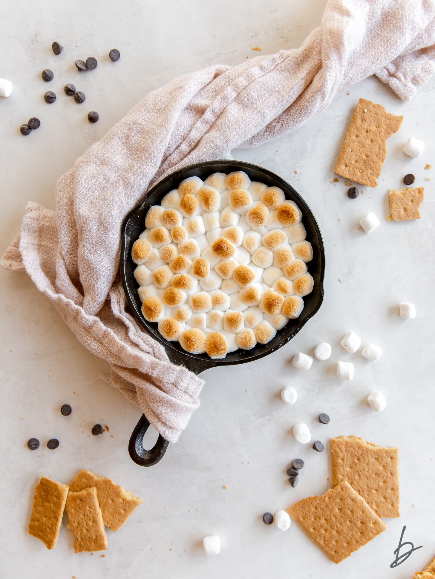 smores dip in cast iron skillet on striped kitchen towel, graham cracker rectangles