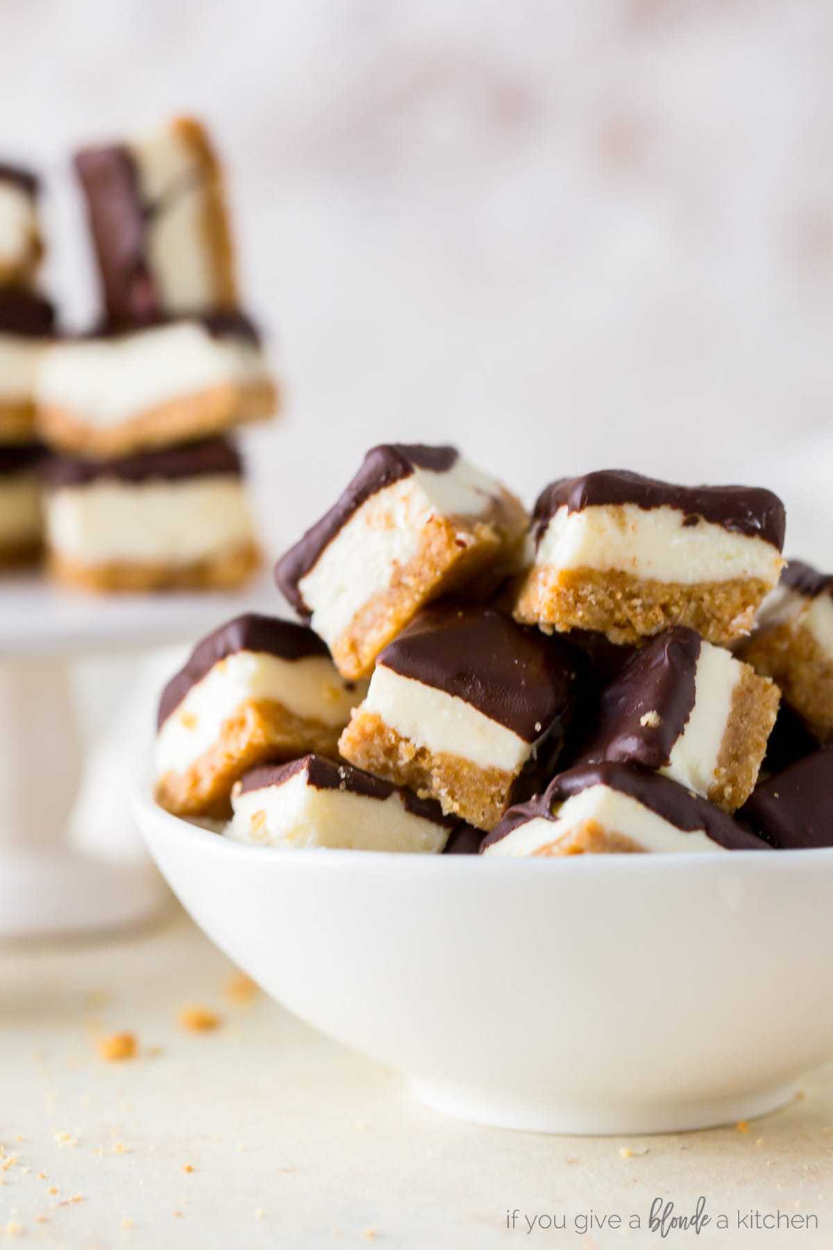 small white bowl filled with mini cheesecake bites layered with graham cracker, cheesecake and chocolate