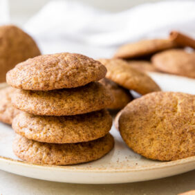 stack of pumpkin snickerdoodles on a white round plate with more cookies next to stack