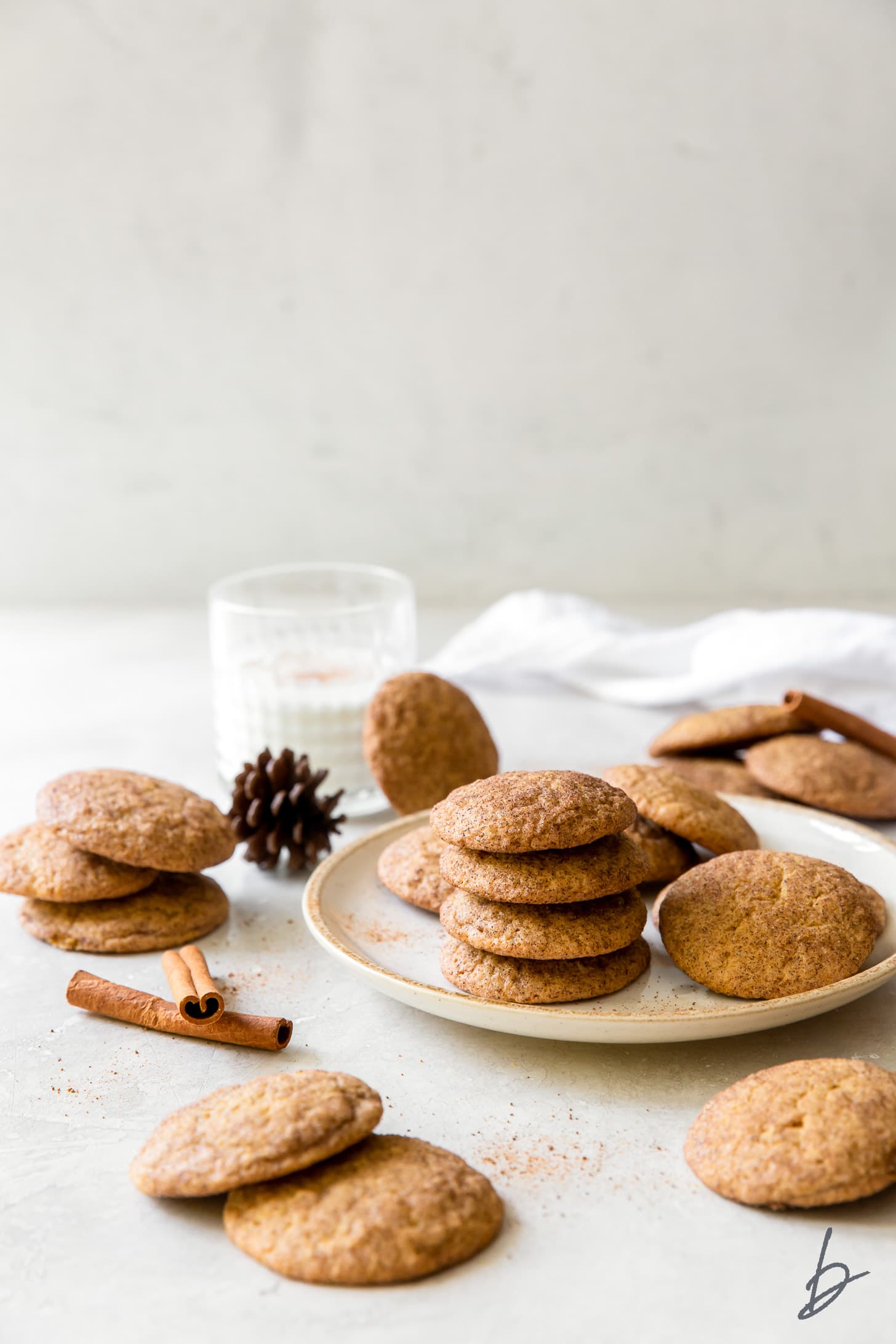 pumpkin snickerdoodles on a plate and around a plate with cinnamon sticks, milk glass behind plate