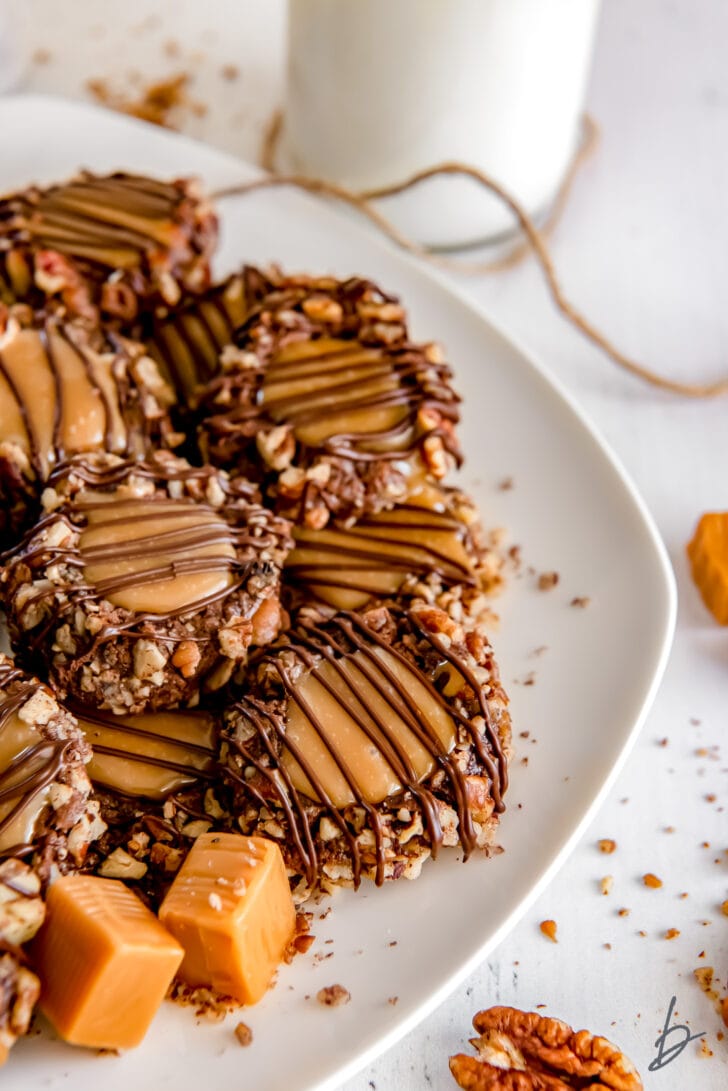 turtle thumbprint cookies with pecans and chocolate drizzle on a white plate with caramel candies