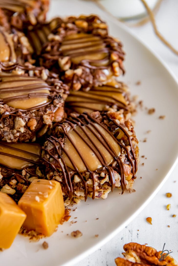plate of turtle thumbprint cookies with chopped pecans, caramel center and chocolate drizzle