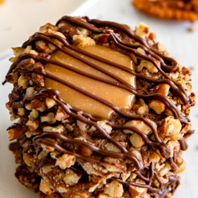 stack of turtle thumbprint cookies and top cookie shows chopped pecans, caramel center and chocolate drizzle on top