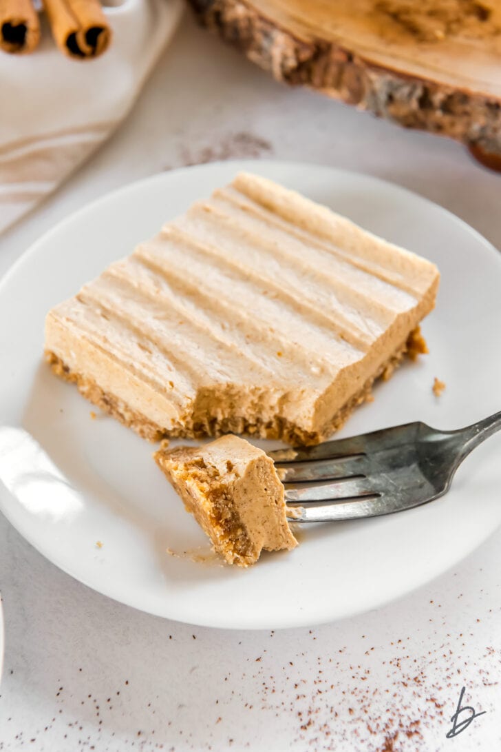no bake pumpkin cheesecake bar on a white round plate with fork taking bite