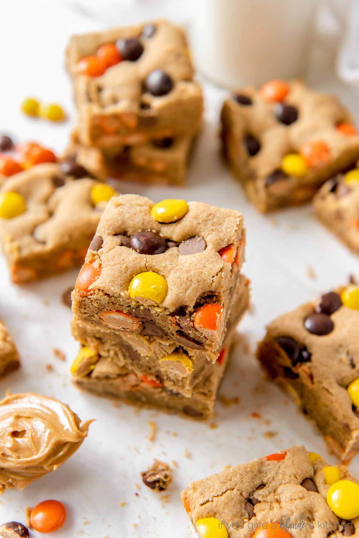 stack of reeses pieces peanut butter blondies on parchment paper next to more blondies