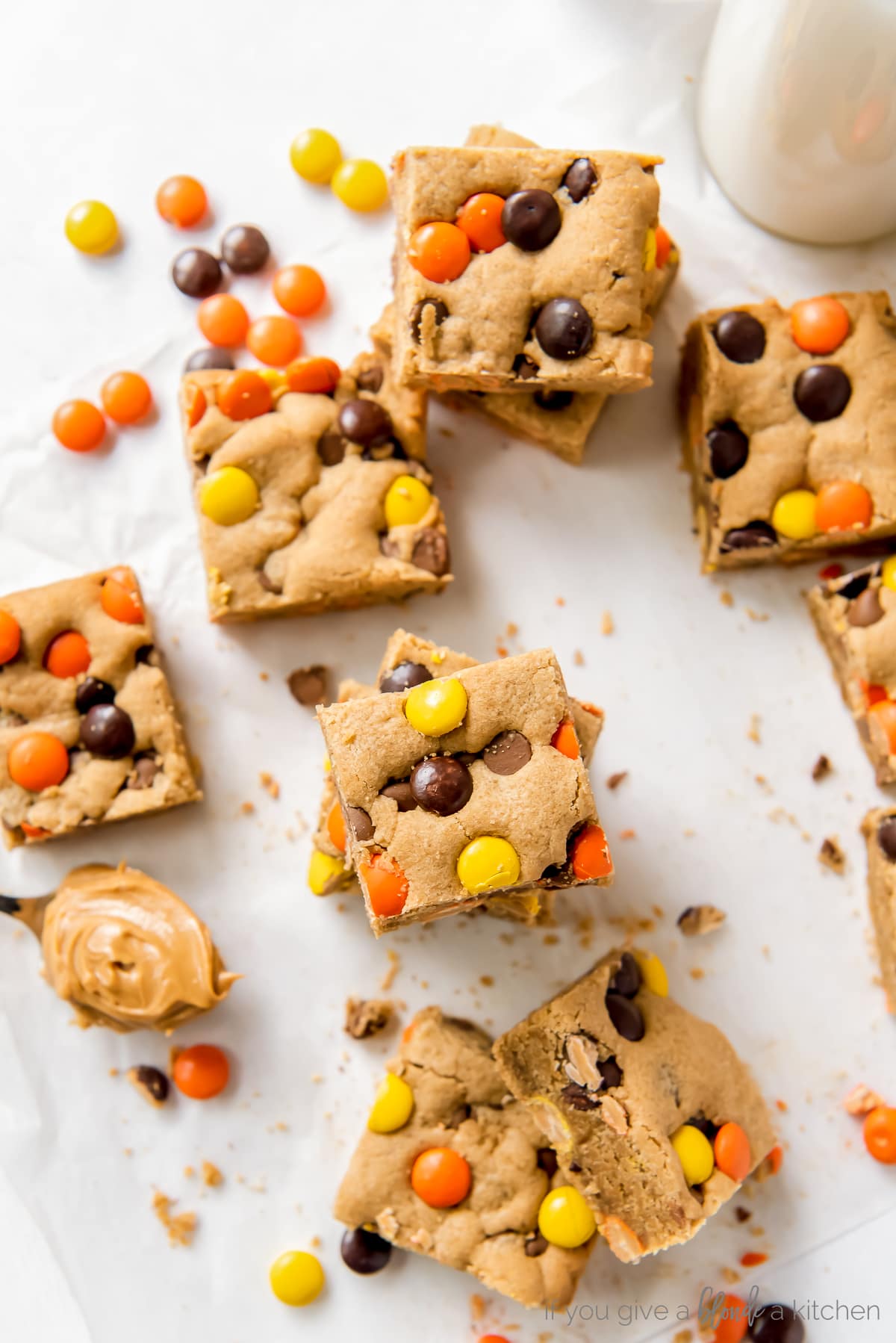 reeses pieces peanut butter blondies on parchment paper next to more reeses pieces candies and spoon of peanut butter