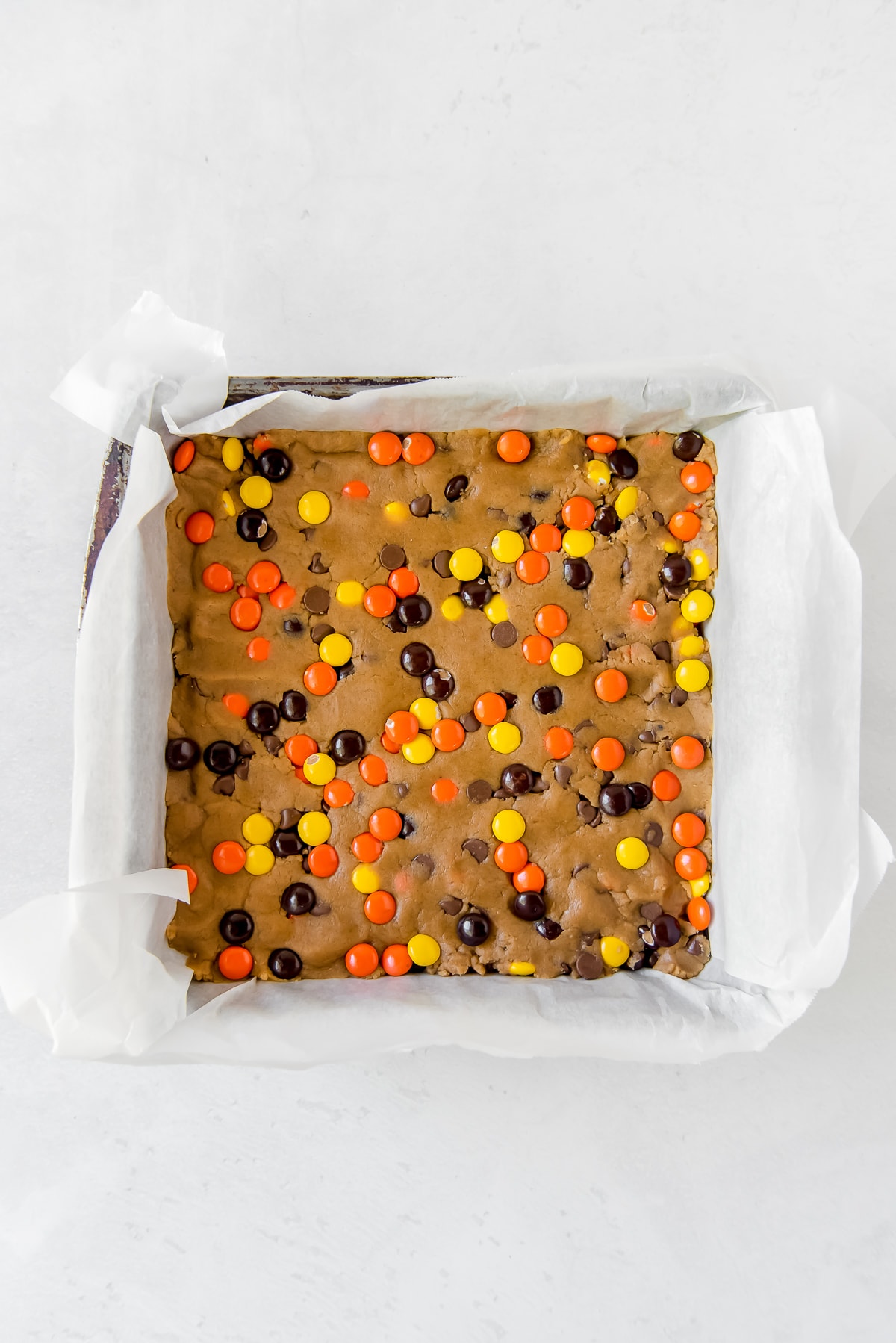 reeses pieces peanut butter blondies dough presses into parchment-lined square baking pan