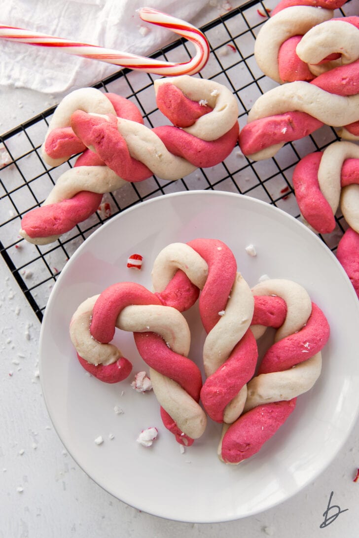three twist candy canes on a white round plate on a wire cooling rack with more cookies