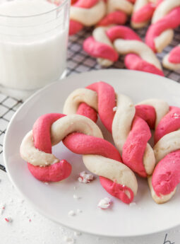 three twist candy cane cookies on white round plate next to glass of milk