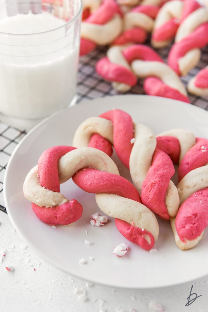 three twist candy cane cookies on white round plate next to glass of milk
