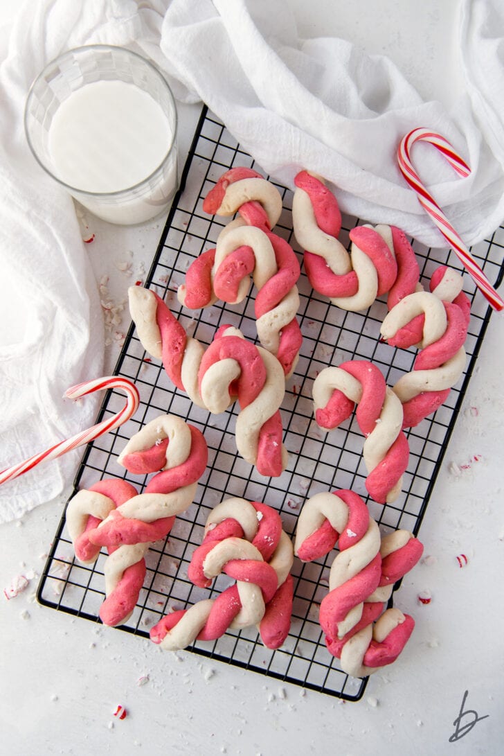 twist candy cane cookies on wire cooling rack next to glass of milk and candy canes