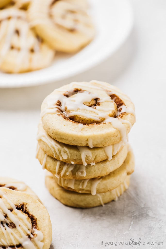 stack of cinnamon roll cookies with icing. Plate of cookies behind stack