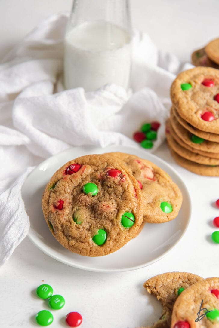 M&M christmas cookies on white round plate next to more cookies and white kitchen cloth