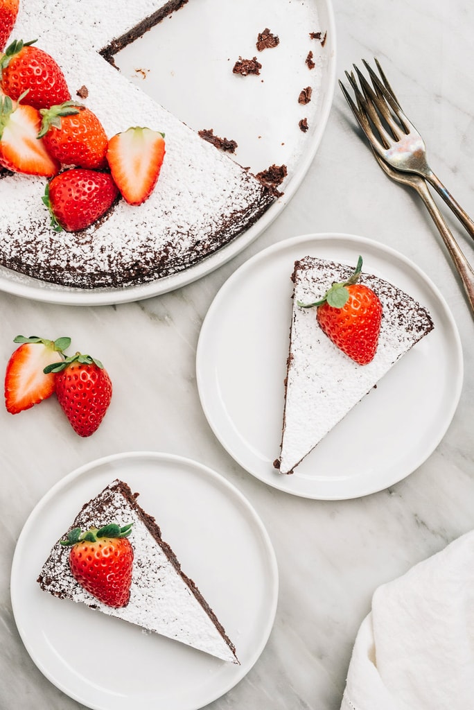 slices of flourless chocolate cake on white round plates with strawberries