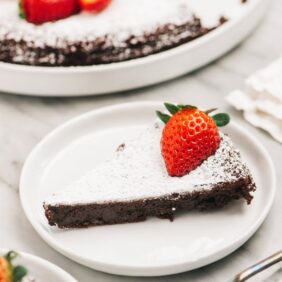 slice of flourless chocolate cake with powdered sugar and strawberry on white round plate