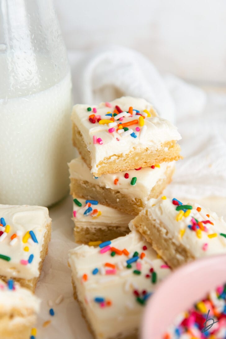 stack of three sugar cookie bars topped with frosting and rainbow sprinkles next to a milk bottle