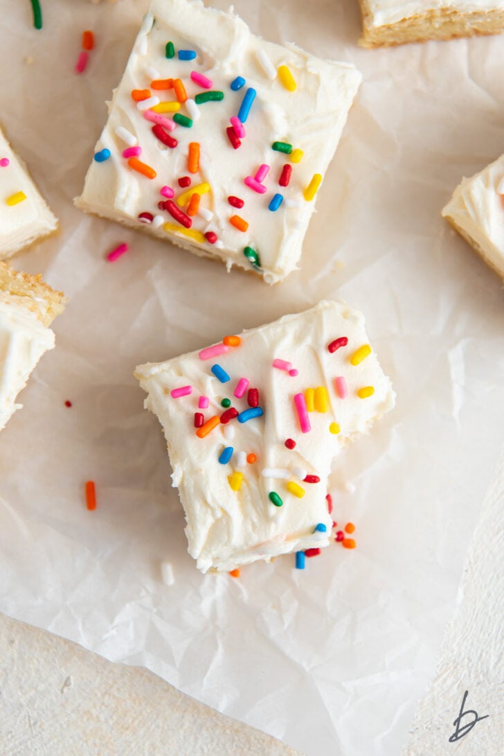 sugar cookie bar topped with frosting and rainbow sprinkles and a bite taken out of the bar