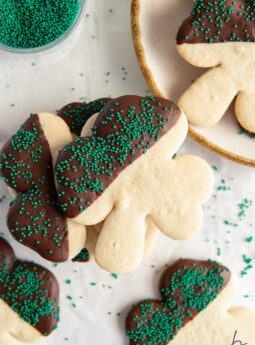 chocolate dipped shamrock sugar cookie with green sprinkles on top of more shamrock cookies