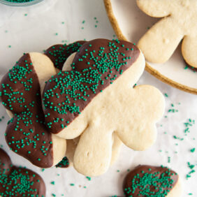 chocolate dipped shamrock sugar cookie with green sprinkles on top of more shamrock cookies