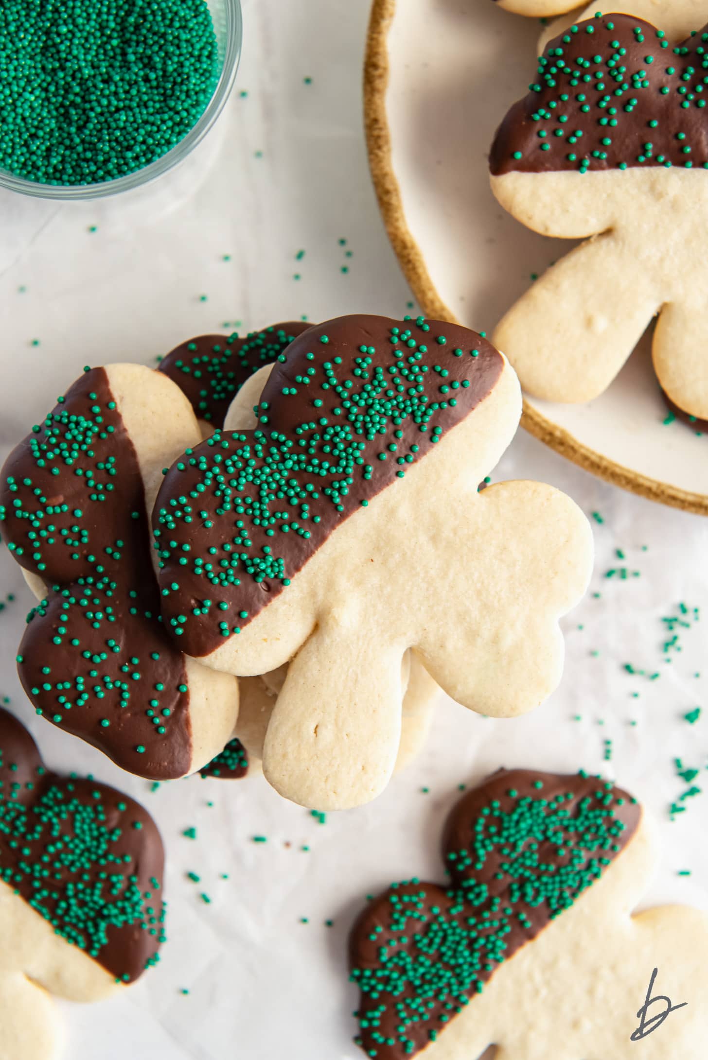 chocolate dipped shamrock sugar cookie with green sprinkles on top of more shamrock cookies