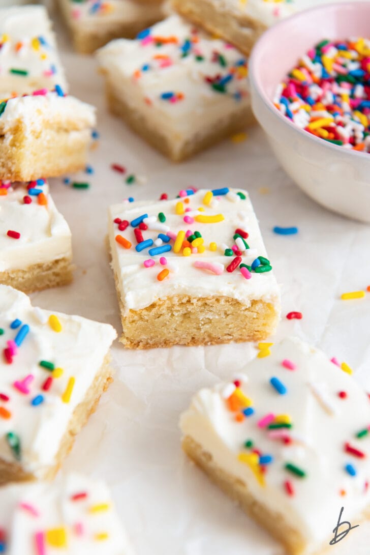 sugar cookie bars with frosting and rainbow sprinkles next to more bars