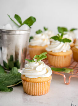 mint julep cupcake with frosting and mint leave garnish in front of silver mint julep cup and more cupcakes