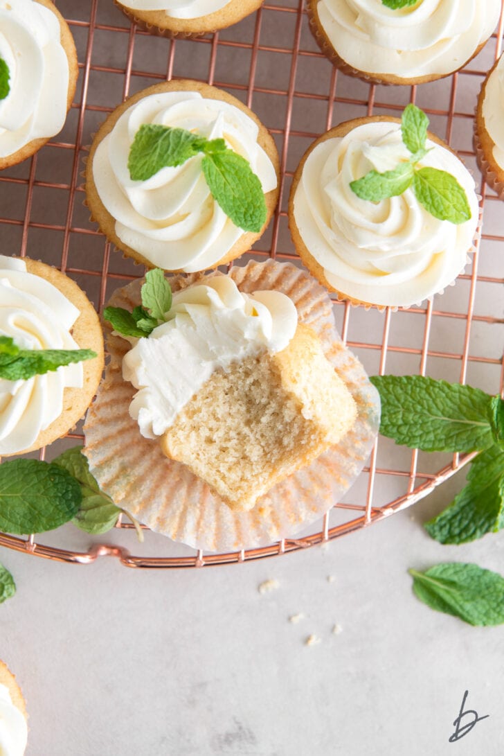 mint julep cupcakes and mint leaves on round rose gold wire rack and one cupcake on its side with a bite