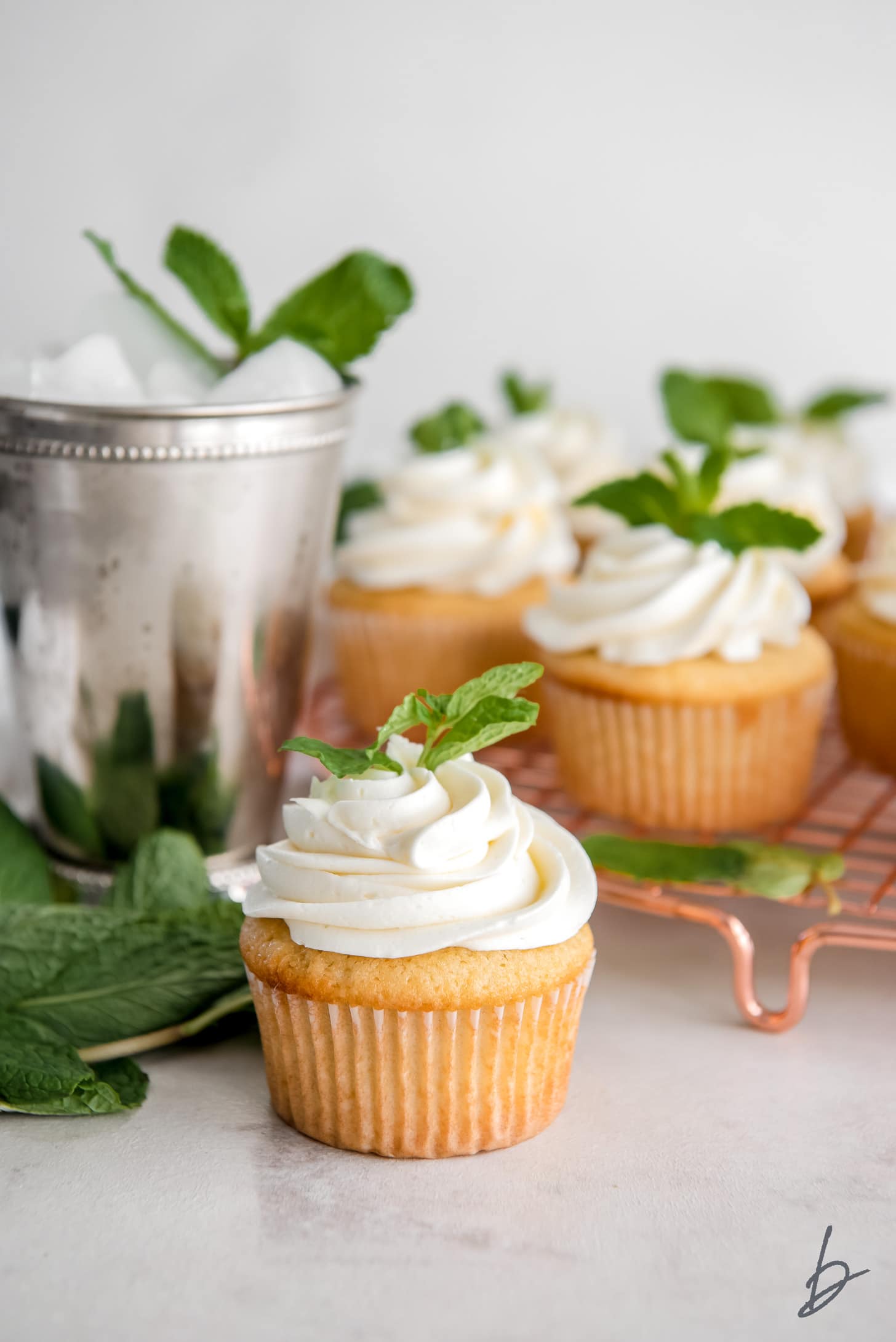 mint julep cupcake with frosting and mint leave garnish in front of silver mint julep cup and more cupcakes