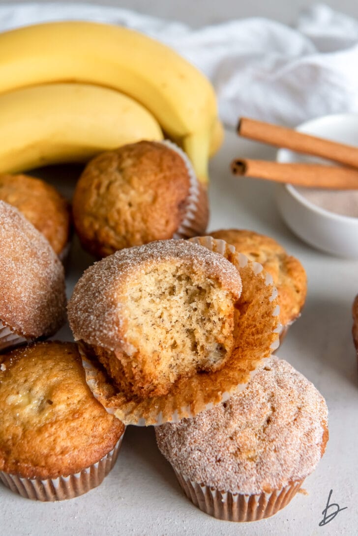 banana cinnamon muffin with a bite on open paper line on top of more muffins
