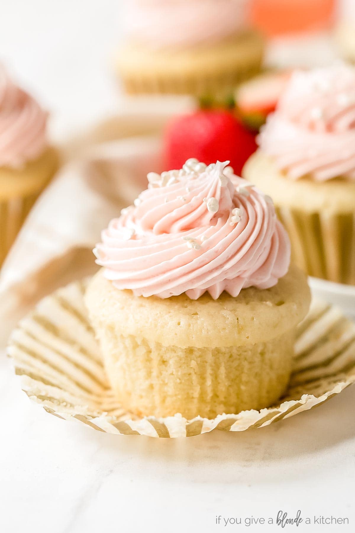 strawberry moscato cupcakes recipe with bite taken out of cupcake sitting on cupcake liner with strawberries