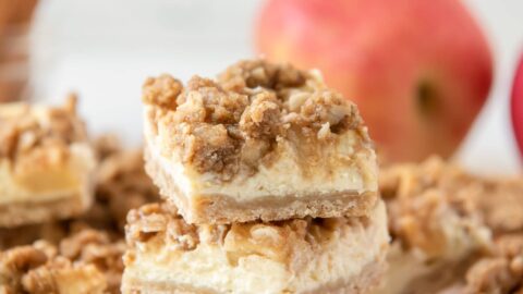 stack of three apple cheesecake bars showing layers of shortbread crust, cheesecake, apples and streusel