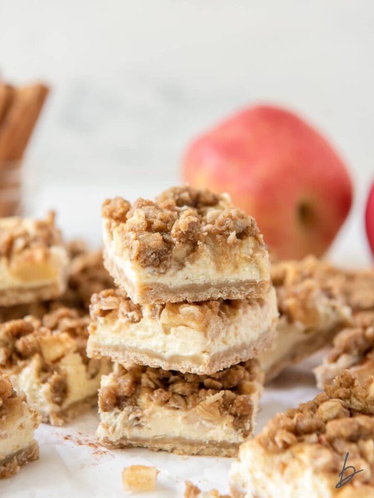 stack of three apple cheesecake bars showing layers of shortbread crust, cheesecake, apples and streusel