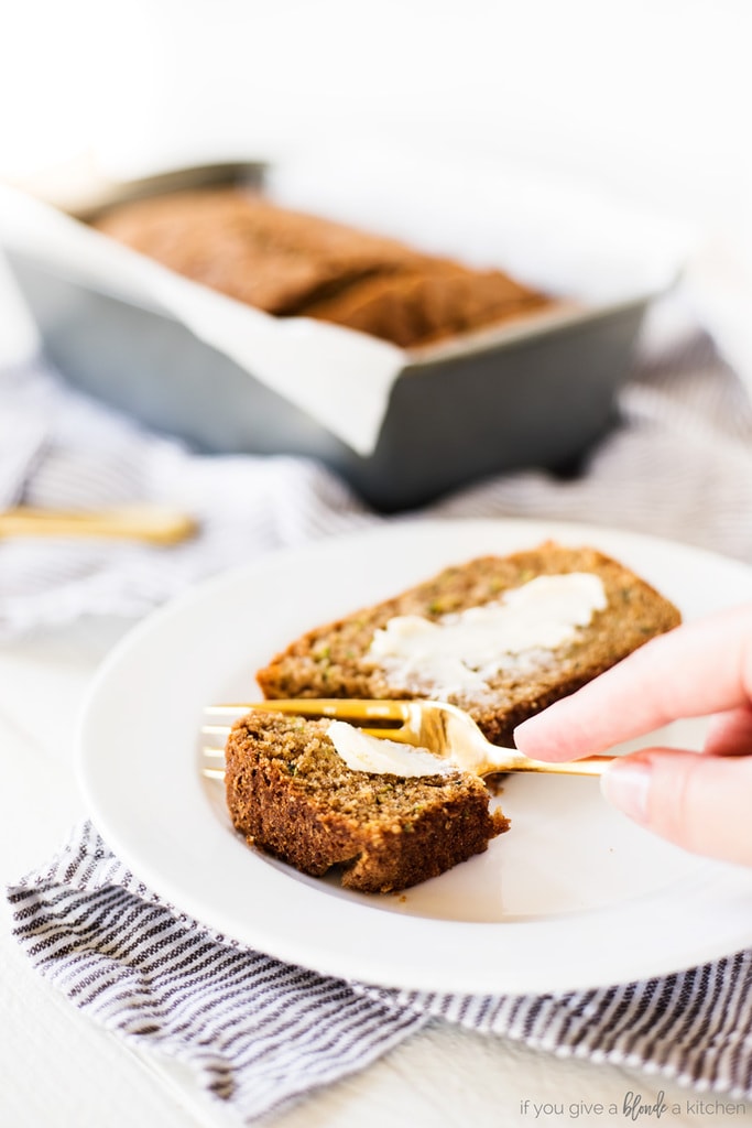 zucchini bread slice on white round plate with butter and gold fork