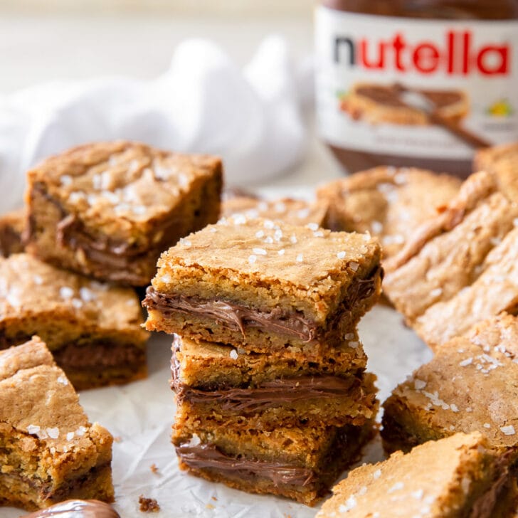 stack of three nutella stuffed blondies surrounded by more blondies and jar of Nutella
