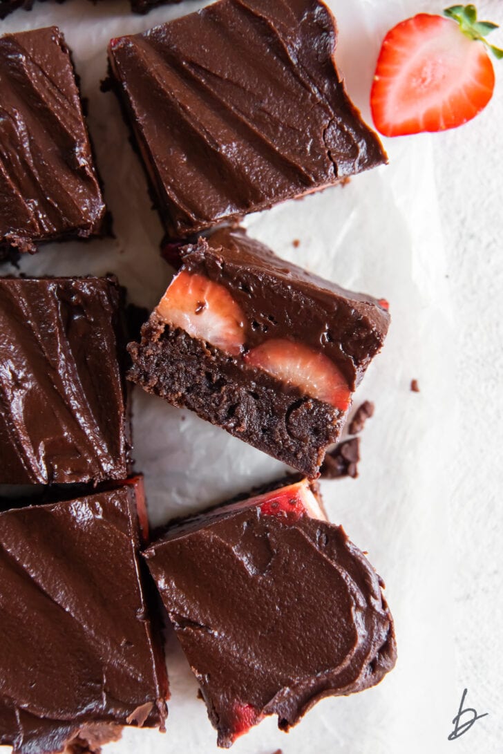 chocolate covered strawberry brownies with ganache and one brownie on its side showing strawberries inside