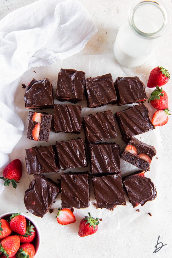 Chocolate covered strawberry brownies cut into squares on parchment paper next to fresh strawberries