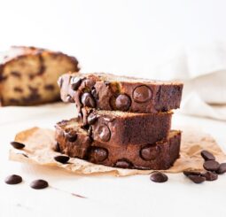Chocolate chip banana bread recipe slice with chocolate chips on parchment paper, white background