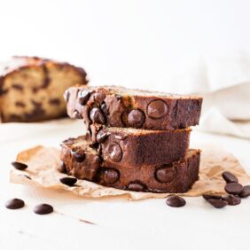 Chocolate chip banana bread recipe slice with chocolate chips on parchment paper, white background
