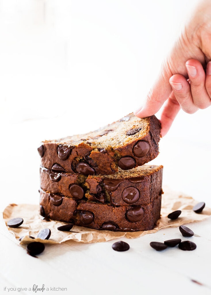 Chocolate chip banana bread recipe hand reaching for slice of banana bread with melted chocolate chips