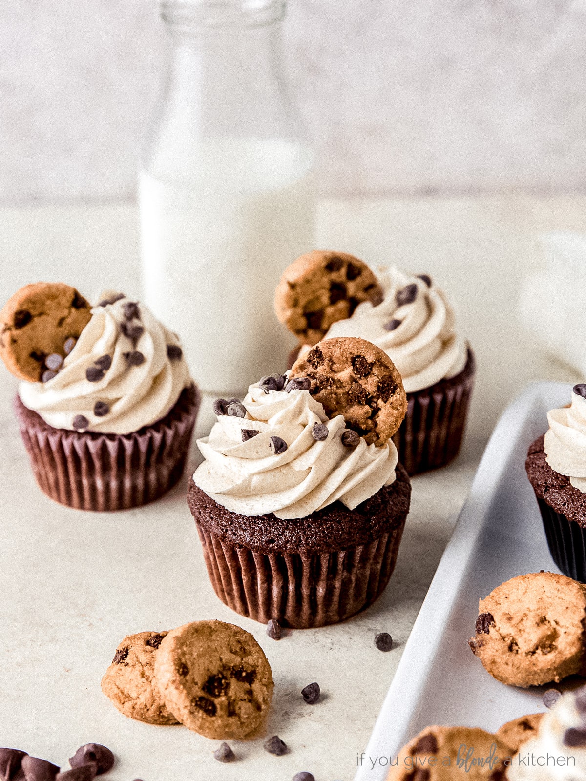 three chocolate chip cookie dough frosting cupcakes in front of tall bottle of milk