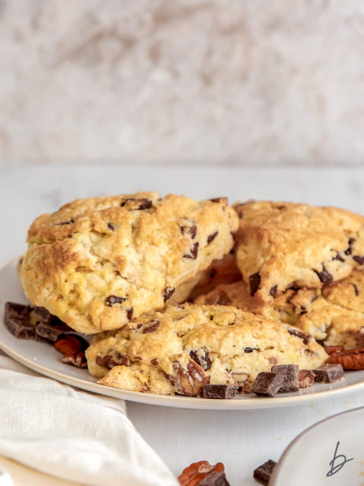 Ina Garten's chocolate pecan scones on plate with chocolate chunks and kitchen towel in front of plate