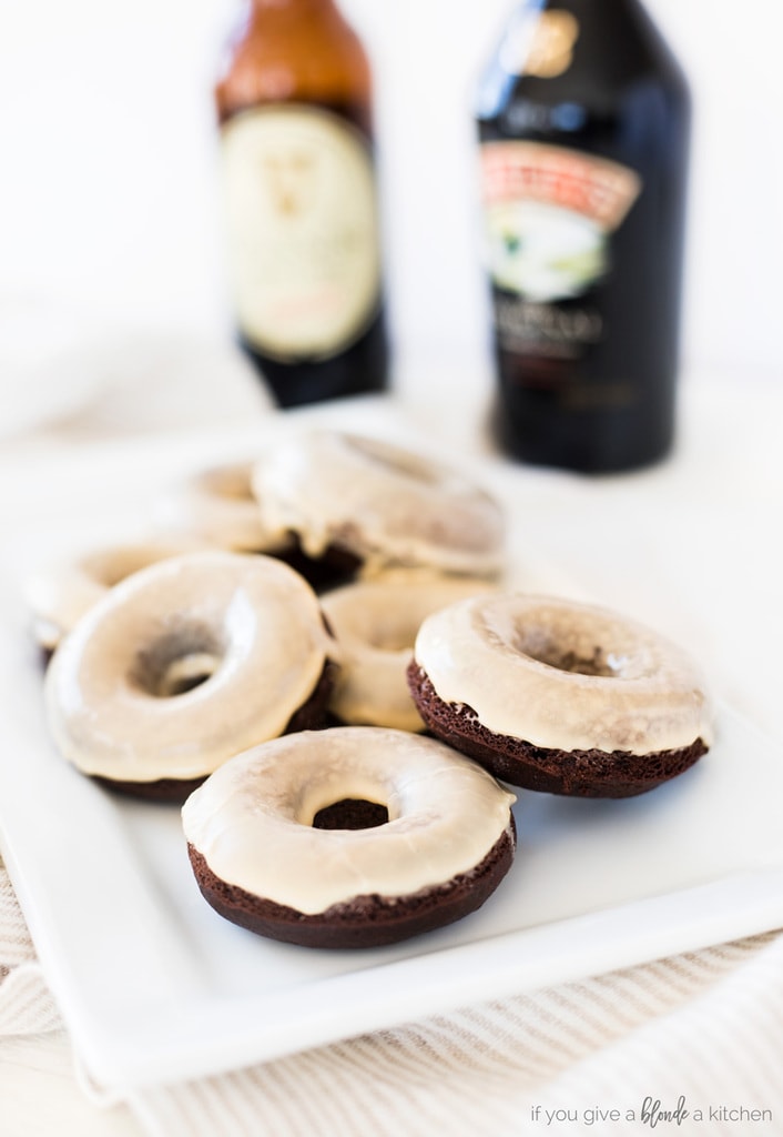 guinness chocolate donuts with baileys irish cream glaze on white plate with light striped kitchen cloth. Bottle of stout beer and Baileys in white background